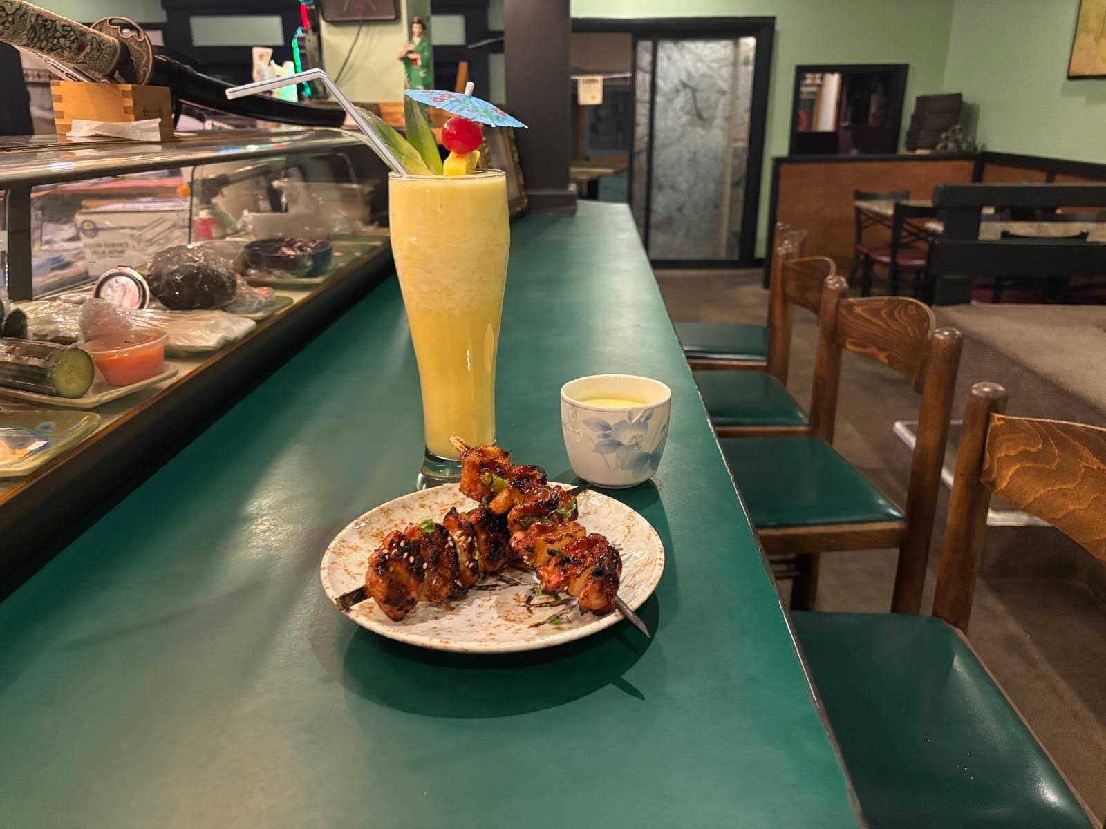 Glazed chicken yakitori skewers and a tropical cocktail with pineapple garnish on Suehiro's green sushi bar counter